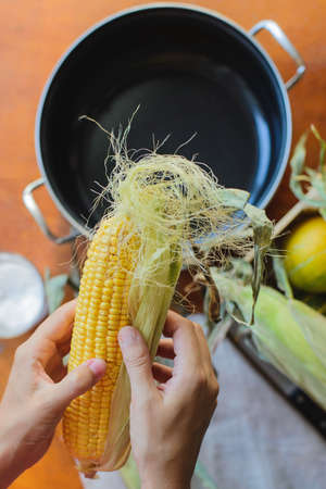 woman prepares corn for cooking in a bowl, top view from selfの写真素材