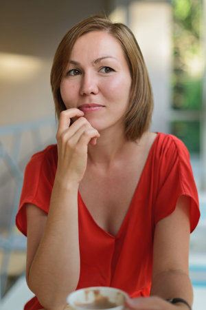 young woman in red dress drinking drink at cafe near window