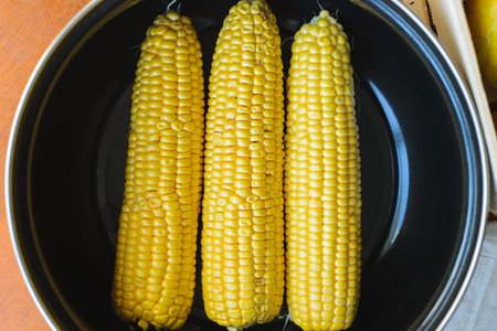 golden corn in black bowl on brown table top viewの写真素材