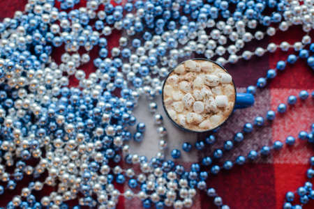 top view cup of cocoa with marshmallows near blue bead on red checkered backgroundの写真素材
