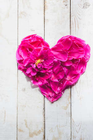 top view of red peonies petals in heart shape as love symbol for wedding or valentines day decorate on wooden board backgroundの写真素材