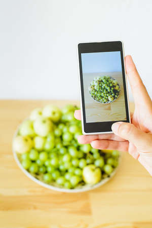 girl shoot photo on phone plate tray with fruit apples and grapesの写真素材