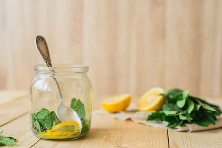 side view of homemade lemonade cooking with yellow lemon, green mint and water in glass jar in wooden interior kitchenの写真素材