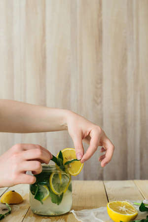 side view of homemade lemonade cooking with yellow lemon, green mint and water in glass jar in wooden interior kitchenの写真素材