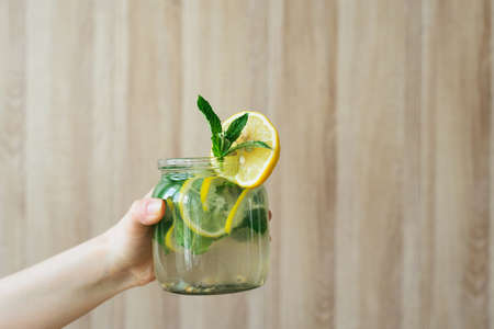 side view of homemade lemonade cooking with yellow lemon, green mint and water in glass jar in wooden interior kitchenの写真素材