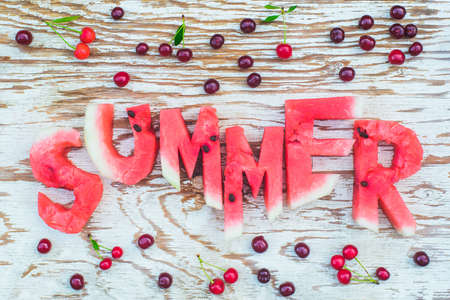 top view flat lay of sliced fresh ripe watermelon summer letters with cherries frame on a white rustic wood board background, fresh outdoors summer conceptの写真素材