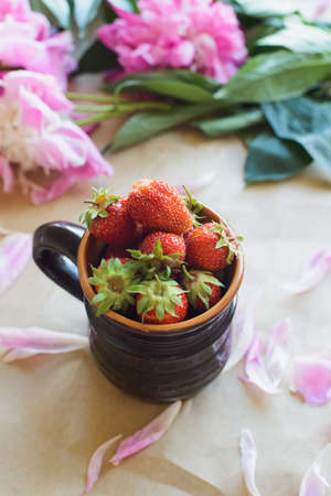 view from above of peonies and strawberries lie on a table on kraft paper photo in natural lightの写真素材