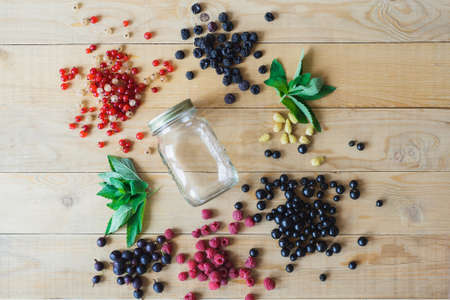 Red, white, black currant, red and black raspberries, white strawberries and mint leaves with glass jar on wooden table as ingredient to healthy cocktail, beverage, yogurt, smoothieの写真素材