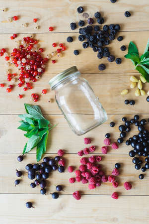 Red, white, black currant, red and black raspberries, white strawberries and mint leaves with glass jar on wooden table as ingredient to healthy cocktail, beverage, yogurt, smoothieの写真素材