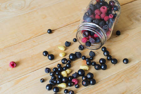 Red, white, black currant, red and black raspberries, white strawberries in glass jar and sprinkle on wooden table as ingredient to healthy cocktail, beverage, yogurt, smoothieの写真素材