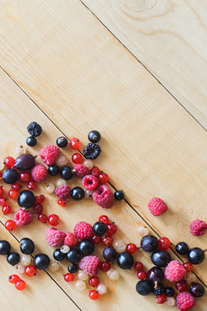 top view of sprinkled red, white, black currant, red and black raspberries, white strawberries on wooden tableの写真素材