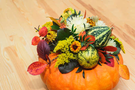 autumn bouquet of decorative pumpkins, flowers and leaves in a vase of orange pumpkin on a wooden tableの写真素材