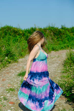 white caucasian blonde girl with colorful long dress dances on a dirt road in fieldの写真素材