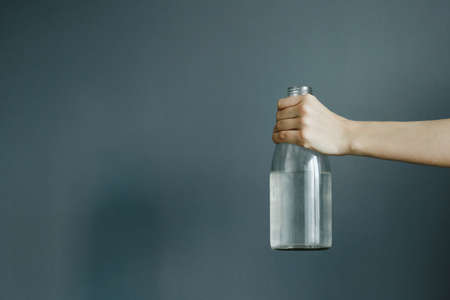 female hand holds bottle with water on gray wall background with copy spaceの写真素材