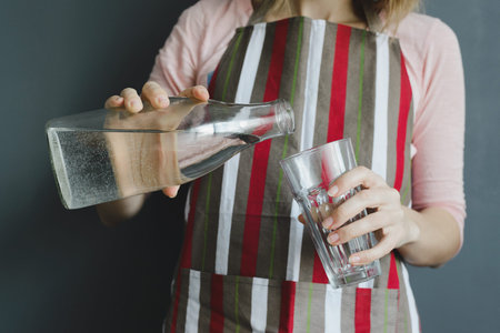 caucasian woman pours water into glass on gray background, stock photo