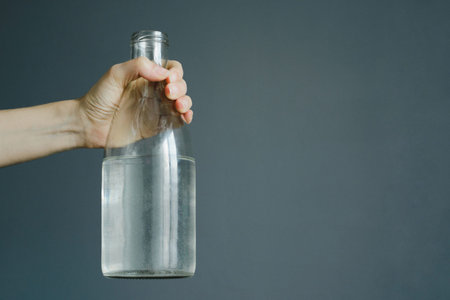womans hand holds bottle with water on gray wall background with copy space, stock photo image