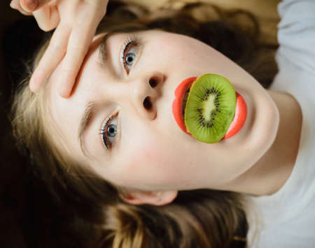 caucasian girl holds kiwi in mouth, stock photo imageの写真素材