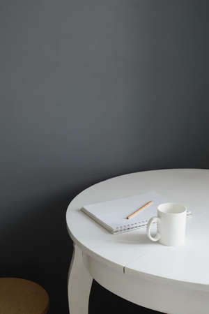 white ceramic coffee cup with notepad and pencil on white wooden table in scandinavian kitchen interiorの写真素材