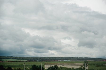 dark dramatic rainy sky clouds over train composition in rural  farm landscape, bad weather in...