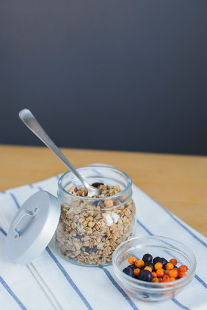 sea buckthorn and blueberry berries, granola with nuts and oat flakes near in glass bowl on striped...