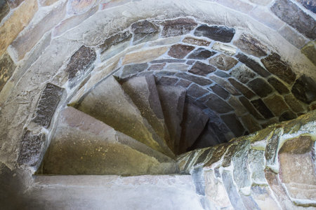 stone spiral staircase with descent down steps and brick wall in castle tower, horizontal stock...