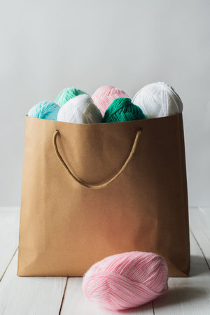 oval acrylic colorful wool yarn thread skeins lying near and into kraft paper brown package on white...