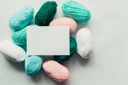 white paper sheet on acrylic soft pastel colored wool yarn thread skeins heap on white background, top view flat lay horizontal stock photo image mockup with copy space for textの写真素材