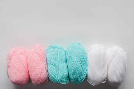 acrylic soft pastel pink, azure and white colored wool yarn thread skeins row on white background,...