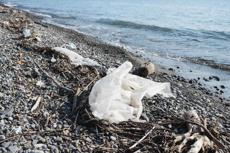 crumpled plastic polyethylene oilcloth, garbage, junk litter, broken tree branches on pebble shore beach, environmental protection concept, horizontal lifestyle stock photo image backgroundの写真素材