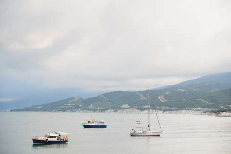 small tourist yachts and fishing boats without people in bad weather in black sea bay on beach, mountains, sity and sky background, horizontal outdoors stock photo imageの写真素材