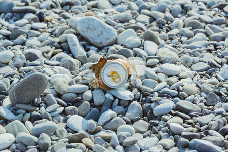 crumpled aluminum metal orange can on pebble beach, environmental protection concept, horizontal lifestyle stock photo image backgroundの写真素材