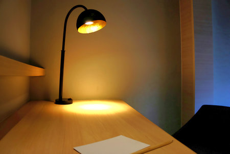 interior of clean office or studying table with  table lamp on a corner side and glows a warm spot light while there's a paper note and a pencil.の写真素材