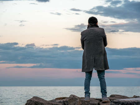 A man stands on the stones and looks at the sea at sunsetの写真素材