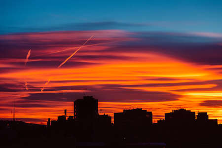 Amazing sunset with orange, pink and red stratus clouds over the city with traces from the planes in the sky. Background for forecast and meteorology concept. Barcelona, Spain.の写真素材
