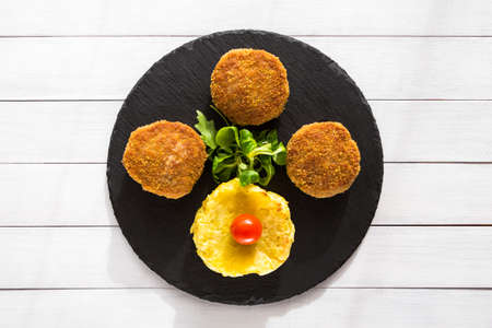 Homemade burgers or cutlets with baked formed potatoes and salad on stone plate and wooden table.の写真素材