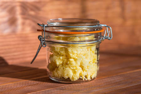 Cheese pate with garlic in a transparent jar on a wooden table at sunny kitchen. Side view.の写真素材