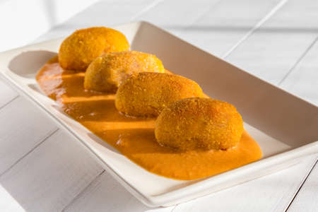 Fried meat croquettes with vegetable cream sauce on white plate at sunny kitchen. Side view on white wooden background.の写真素材