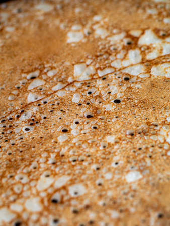 Close-up of small holes during the frying pancakes on iron frying pan. Cooking at home of delicious openwork crepes.の写真素材