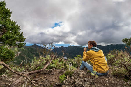 Young male traveler drinks a hot drink in the mountains. Drinking tea or coffee   in the nature.の写真素材