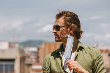 Handsome european man taking off his mask in the sunshine. No more quarantine. Coronavirus is over, freedom concept.の写真素材