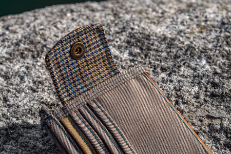 Details and elements of handmade wallet of brown leather and checkered textile on stone background....