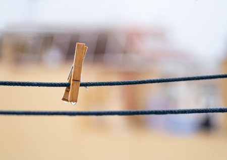 One wooden clothespin on a blue rope with hanging waterdrops after the rain with copy space.