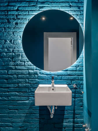 Bathroom with blue bricks wall, square wash basin and round mirror. Minimalist interior.の写真素材