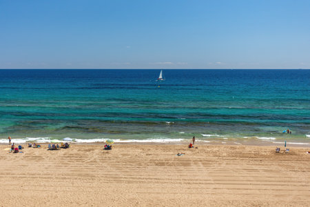 Beach with yellow sand, turquoise water and blue sunny sky. Tourists resting on the beach and looking to the mediteranian sea.の写真素材