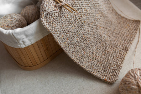 Close-up of knitted texture. Handmade wool scarf of sand color and basket with yarn balls. Selective...