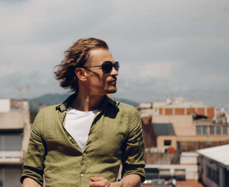 Handsome european man in sunglasses with long hair, standing outdoors and looking to the side.の写真素材