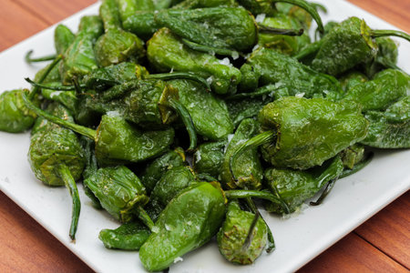 Green pepper Padron baked or fried in the Spanish style on a white plate and wooden background