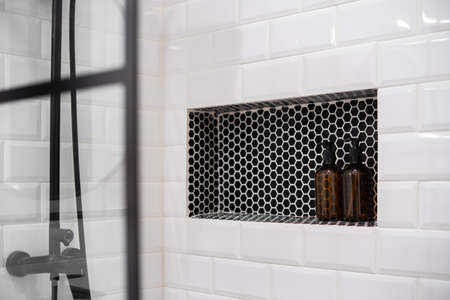Built-in shelf with bottles in modern bathroom. Shower wall with white tiles.の写真素材