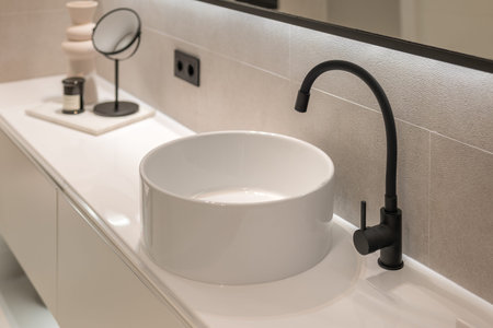 Close-up of modern black faucet and white round sink on pedestal. Modern minimalist style bathroom