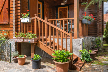 A wooden cottage with stairs and cozy porch. Country house with many plants and trees in european village. Translation on board: welcome.の素材 [FY310192207617]